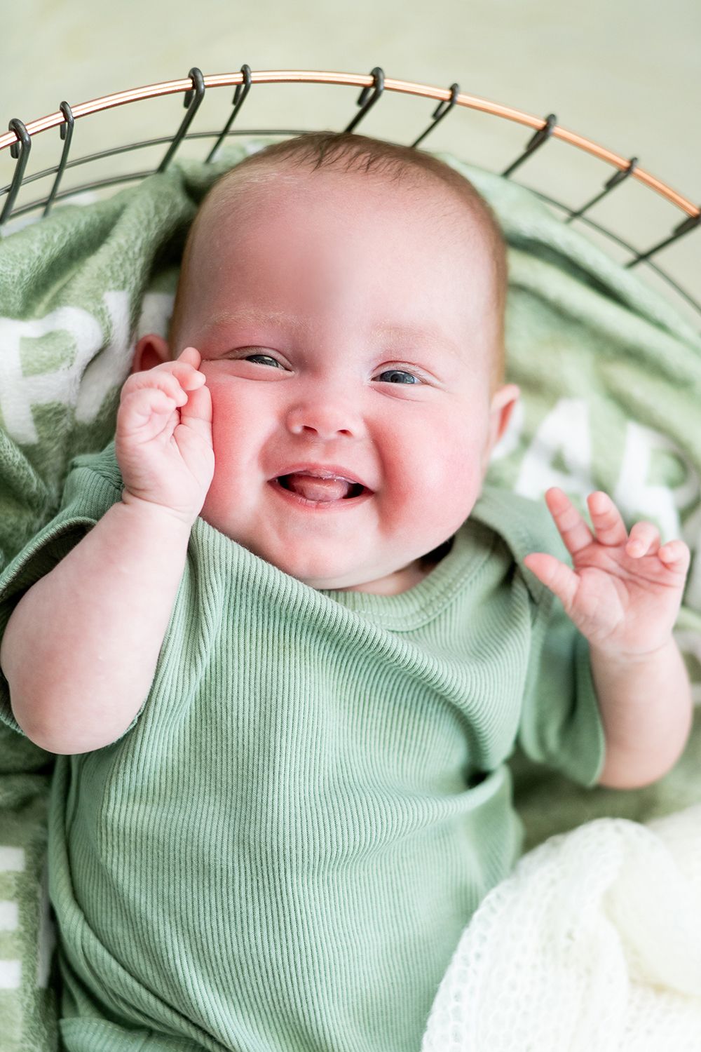 Happy baby in mint green onesie lying down and making playful gestures with hands.