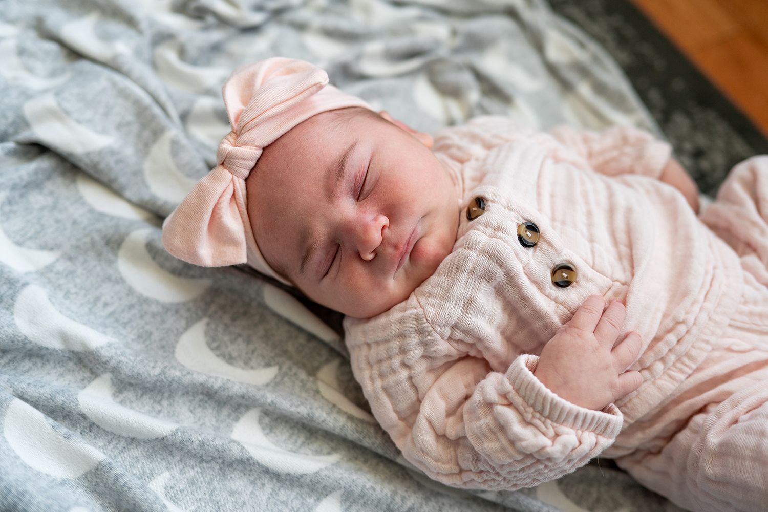Sleeping newborn wearing a soft pink outfit with bear ears on a gray blanket.
