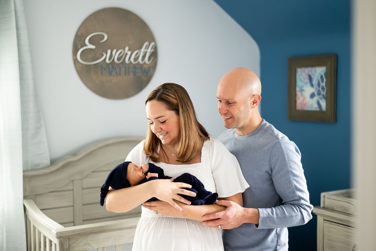 Two people stand lovingly in a nursery with white furniture and blue walls while holding a small black pet.