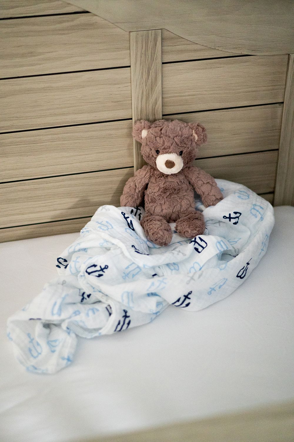 Brown teddy bear sitting on nautical-themed baby blanket with anchor prints against wooden background.