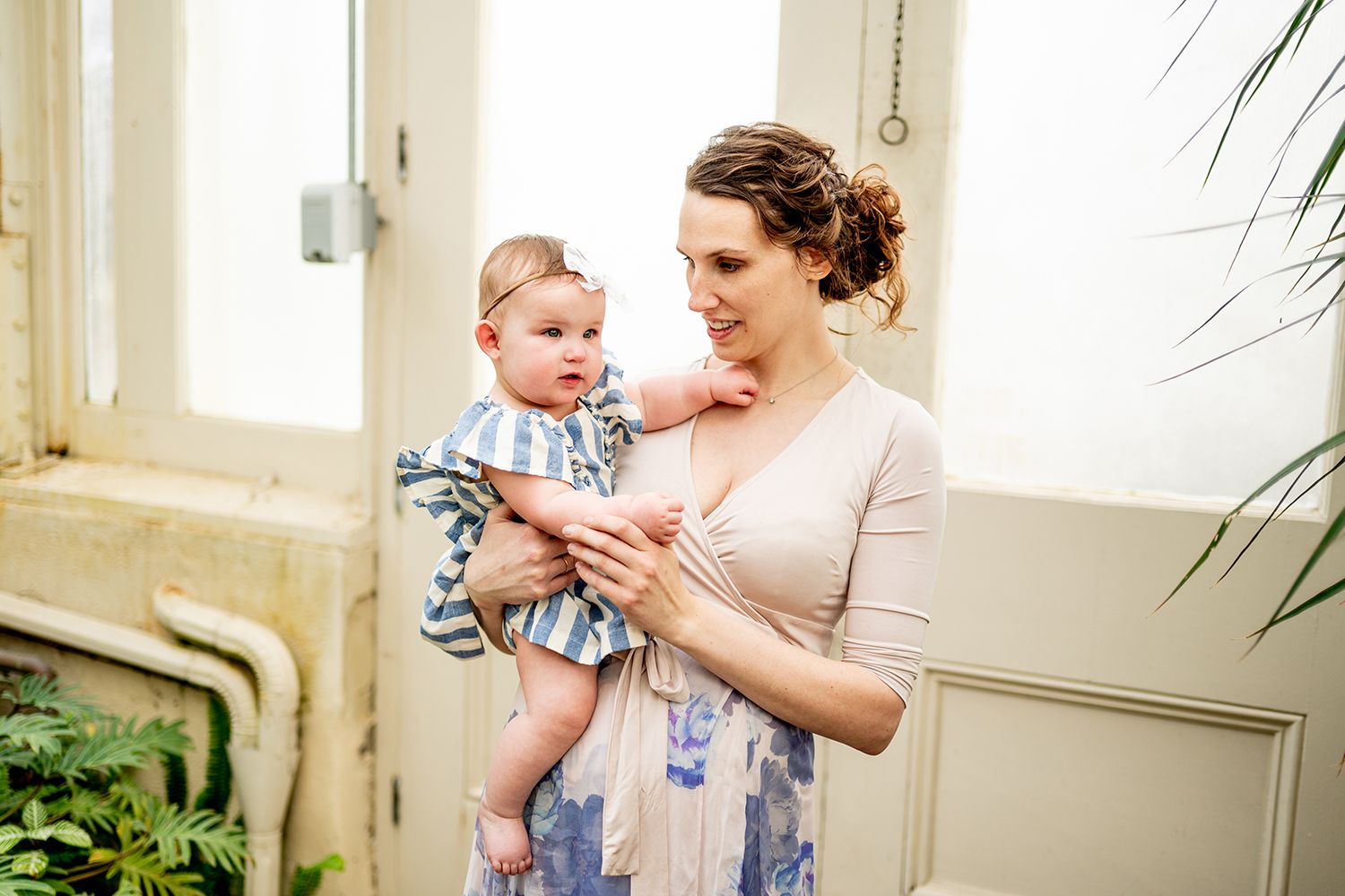 Parent and baby sharing a tender moment near a window in a bright interior setting.