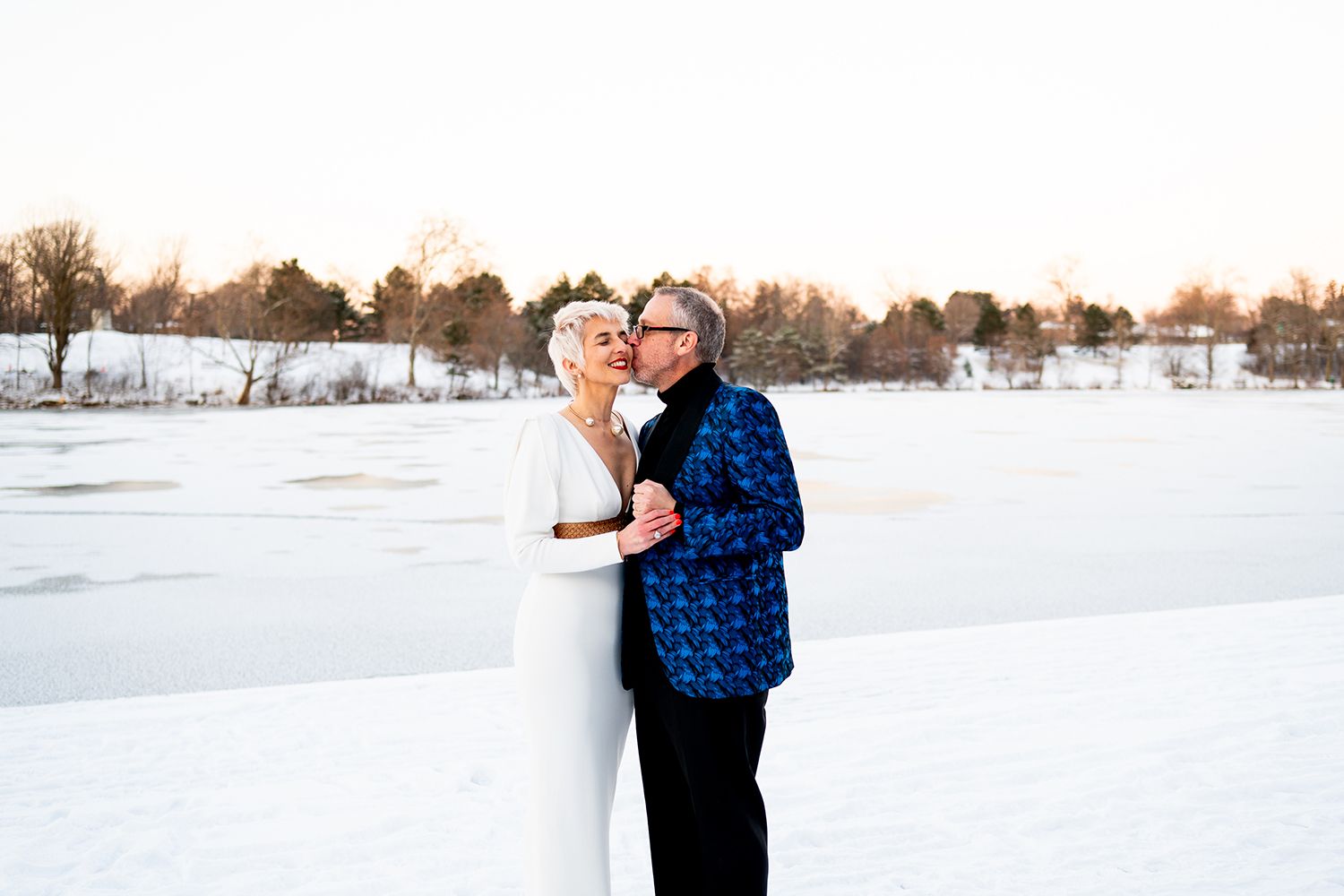 A couple dances together in the snow during sunset, creating a romantic winter scene in an open field.