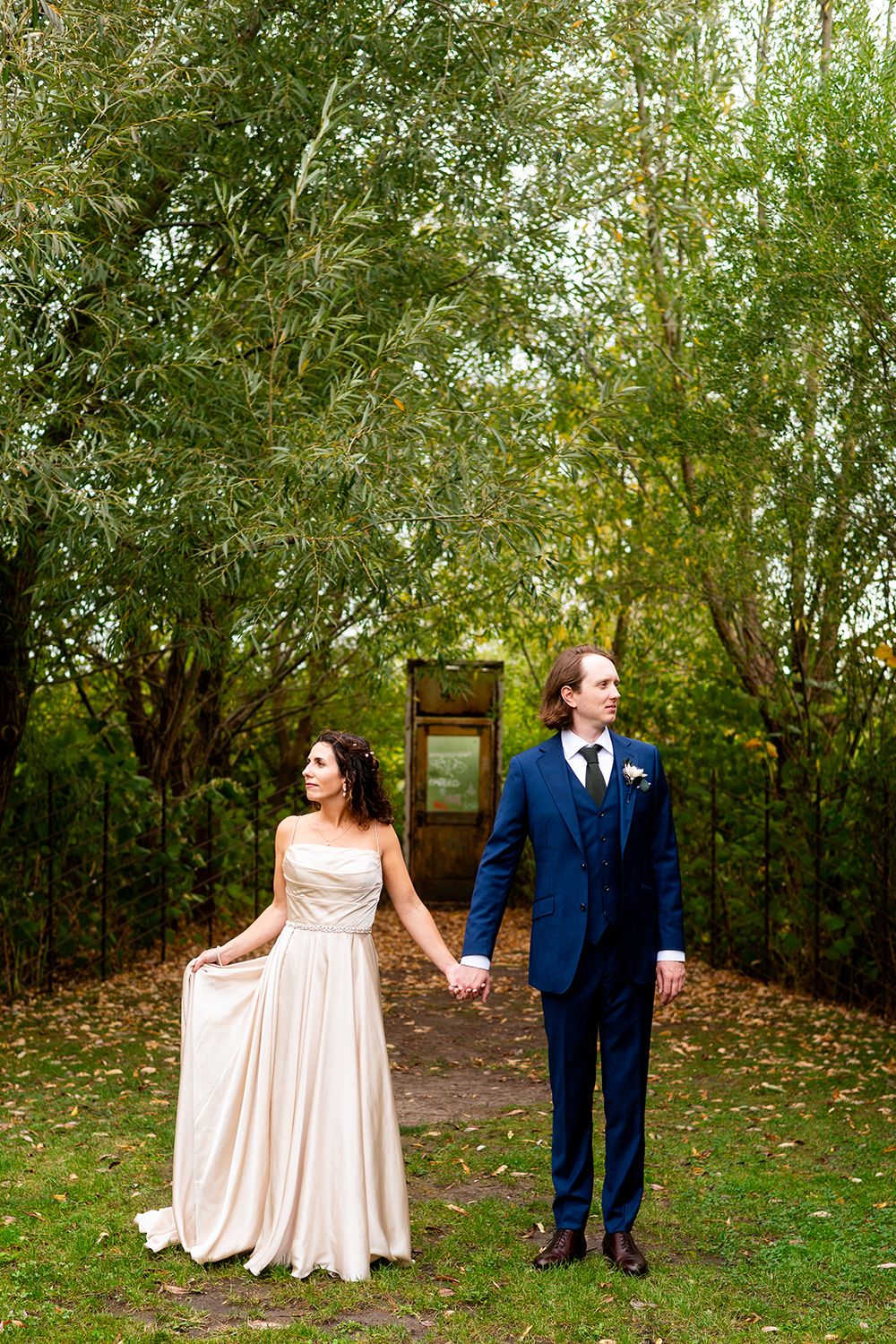 A couple shares a romantic moment in an outdoor garden setting wearing formal attire in blush and navy blue.