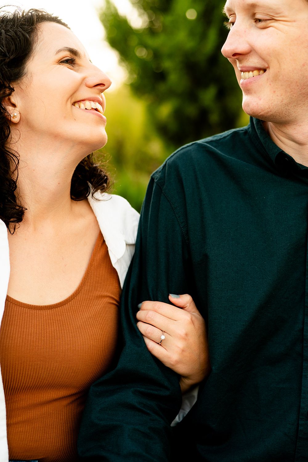 A romantic outdoor portrait of a laughing couple in autumn, with her in brown tops and him in a black sweater.