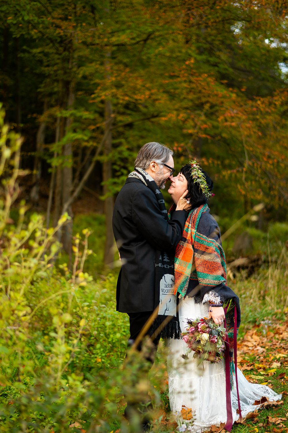 A couple shares a romantic autumn moment among colorful fall foliage in a woodland setting.