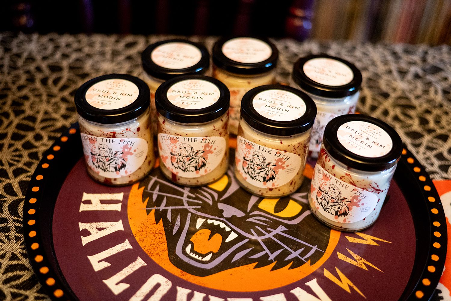Rows of artisanal jars with custom labels displayed on a dark wooden surface in warm lighting.
