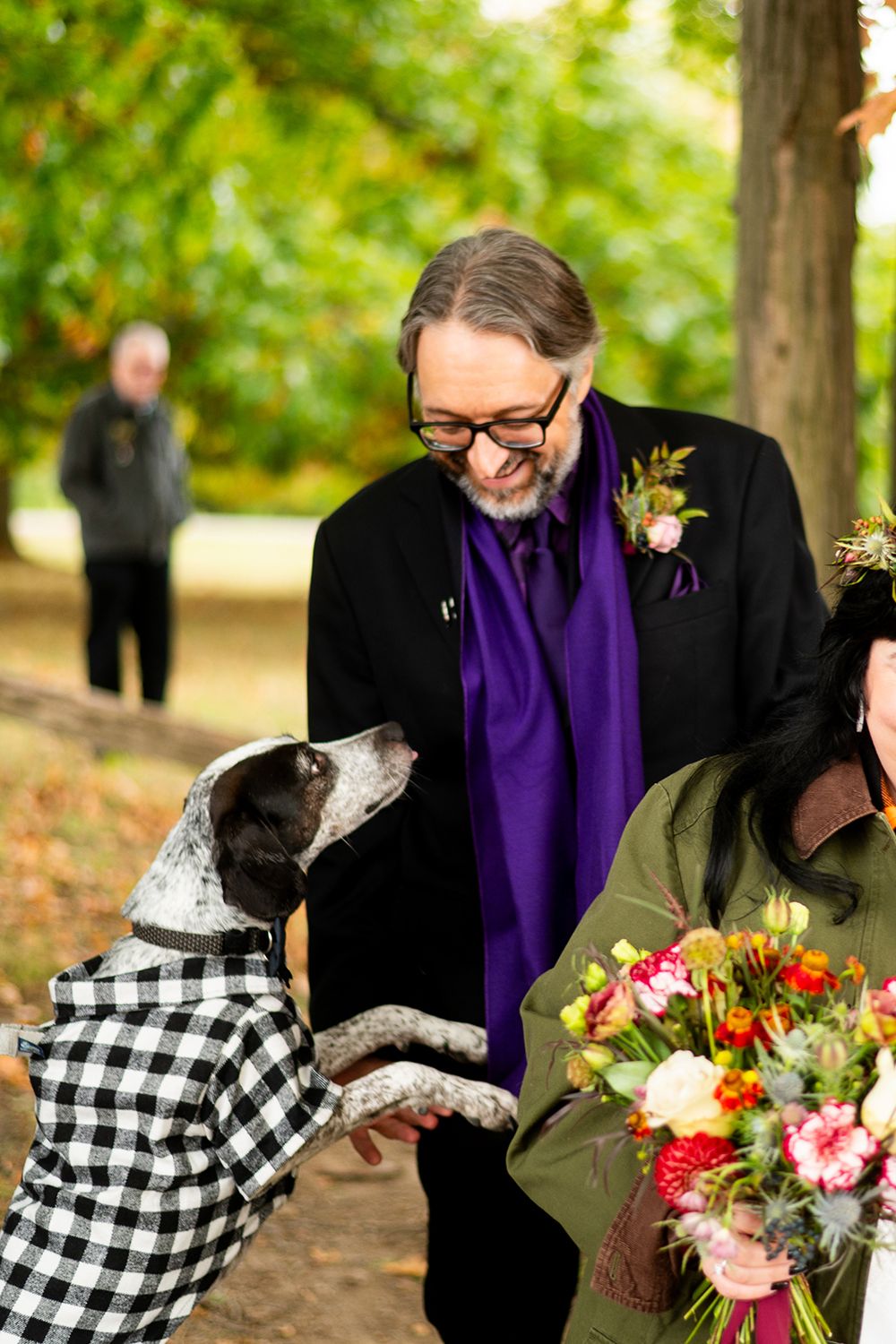 A dog wearing a plaid shirt jacket interacts with attendees at an outdoor autumn event.