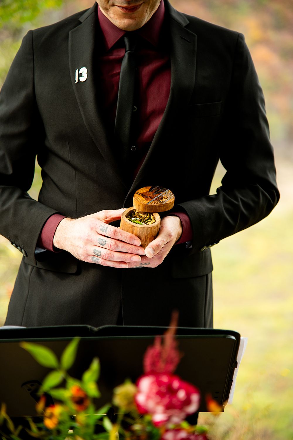 Close up of someone in a black suit and burgundy tie holding a burger during an outdoor event.