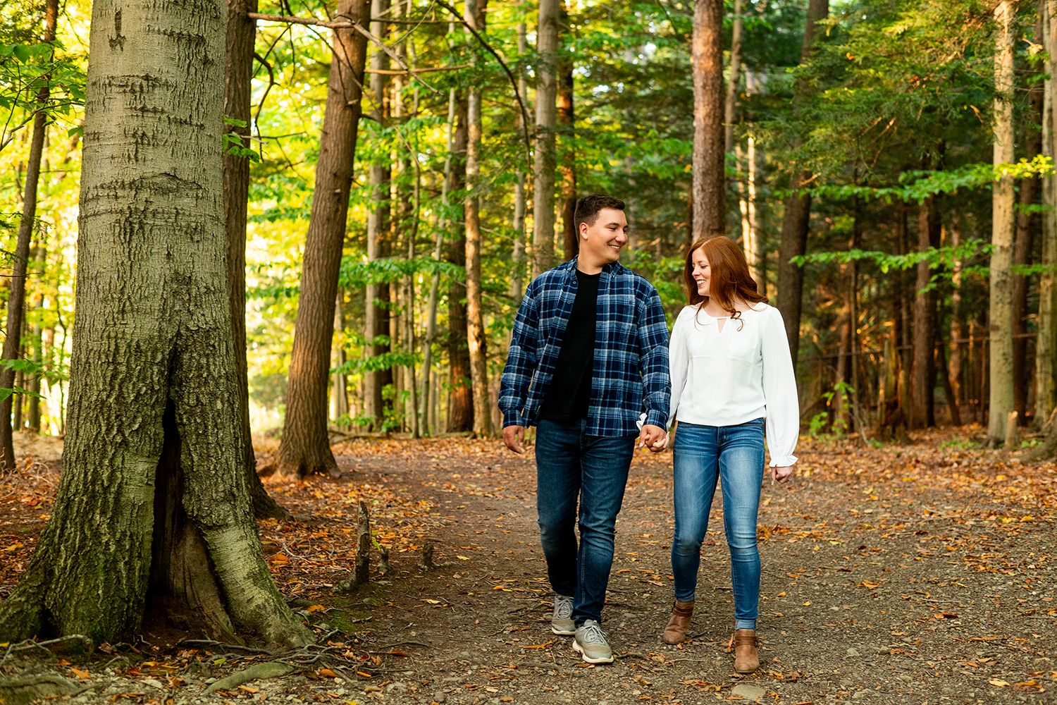 Young couple walking hand in hand on a leaf-covered forest path during autumn season.