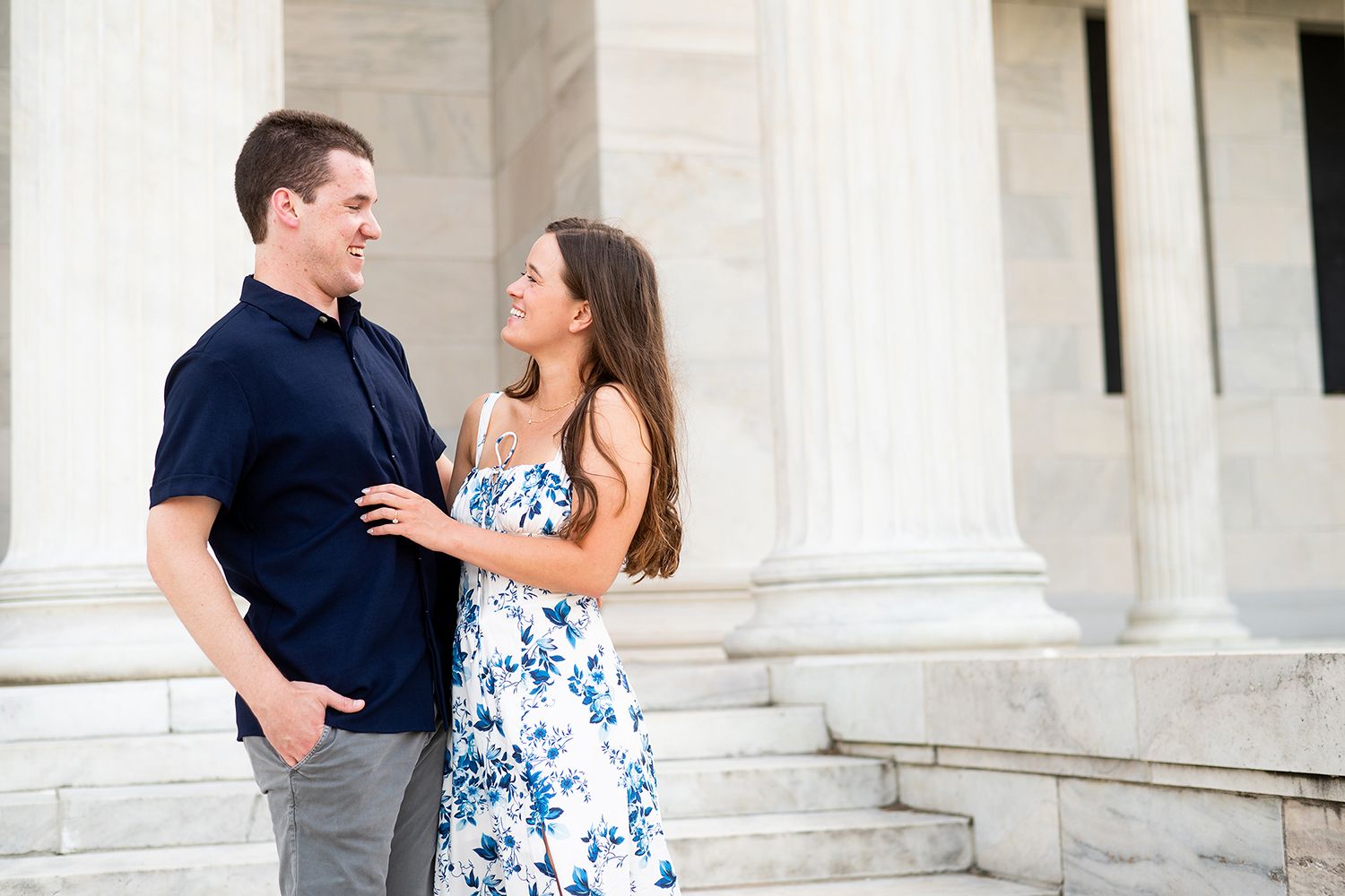 A couple shares a romantic moment on white marble steps in front of classical columns.