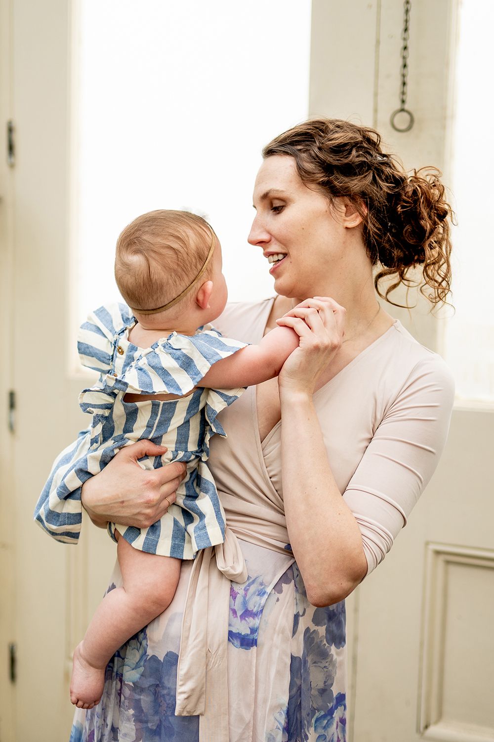A parent holds their small baby wearing blue stripes while both share a joyful moment together at home.