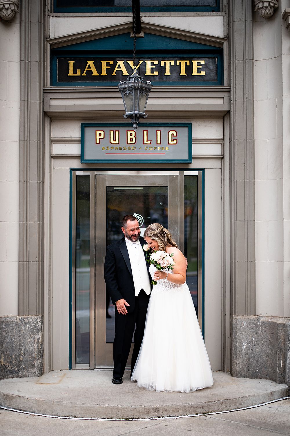 A couple poses together in formal attire outside the entrance of the historic Lafayette Public building.