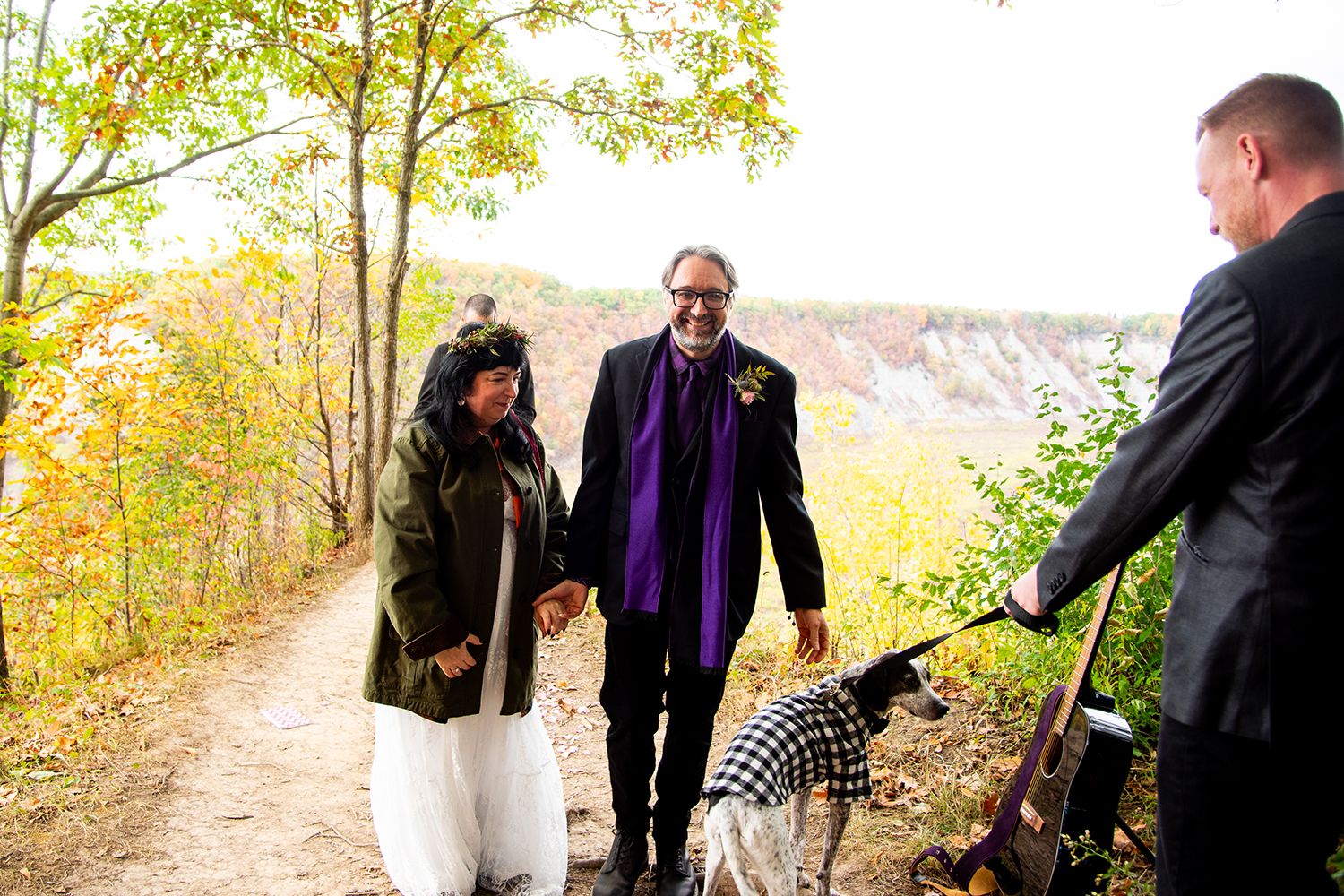 A group of people walk on a winding path through golden autumn foliage in a mountainous landscape.