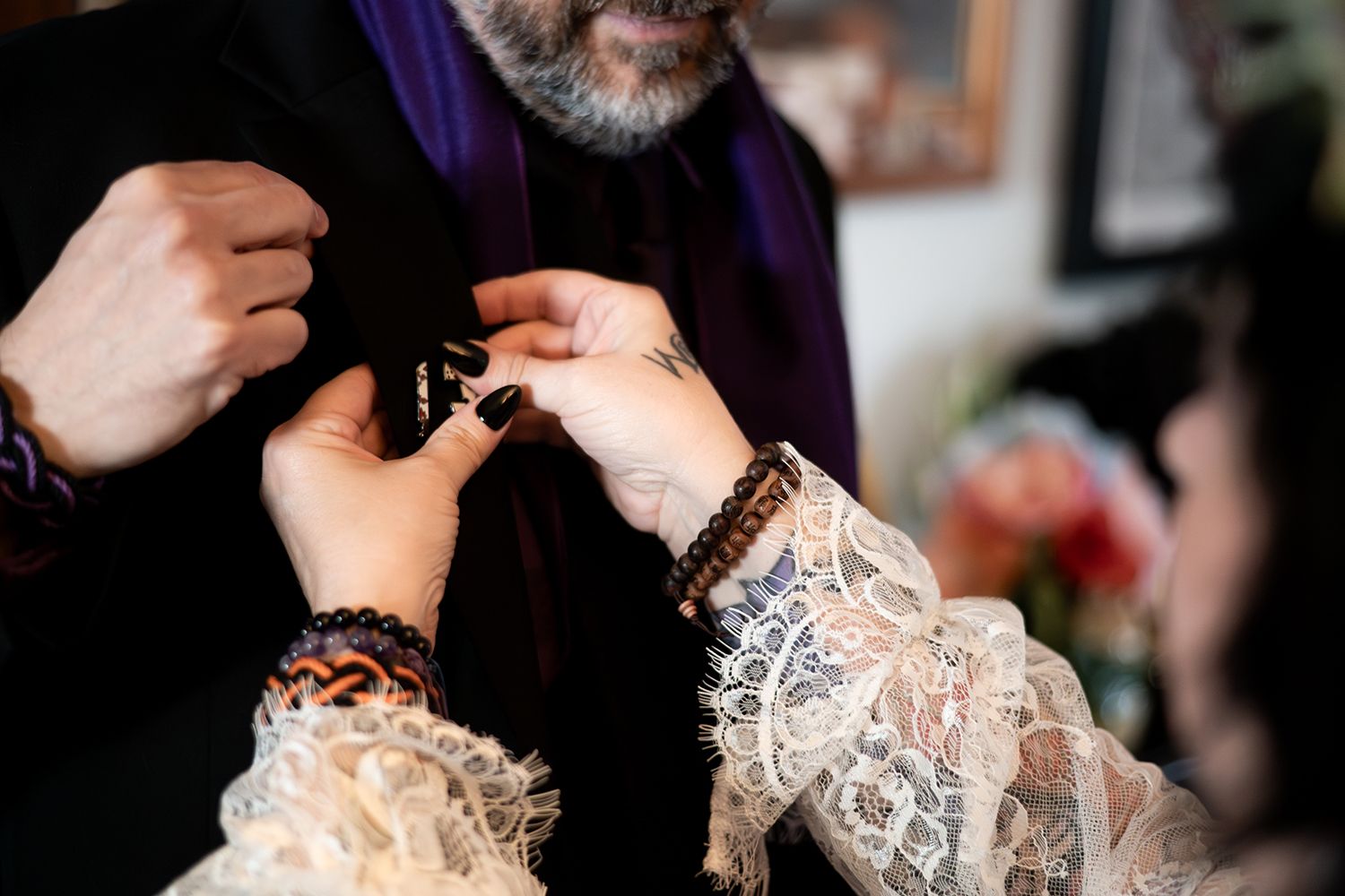 Close-up of hands wearing beaded bracelets working with delicate white lace fabric.