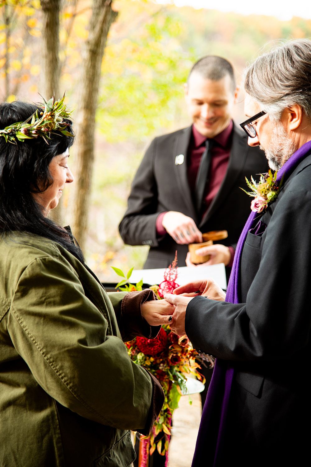 An exchange of rings during a fall wedding ceremony with colorful autumn foliage in the background.