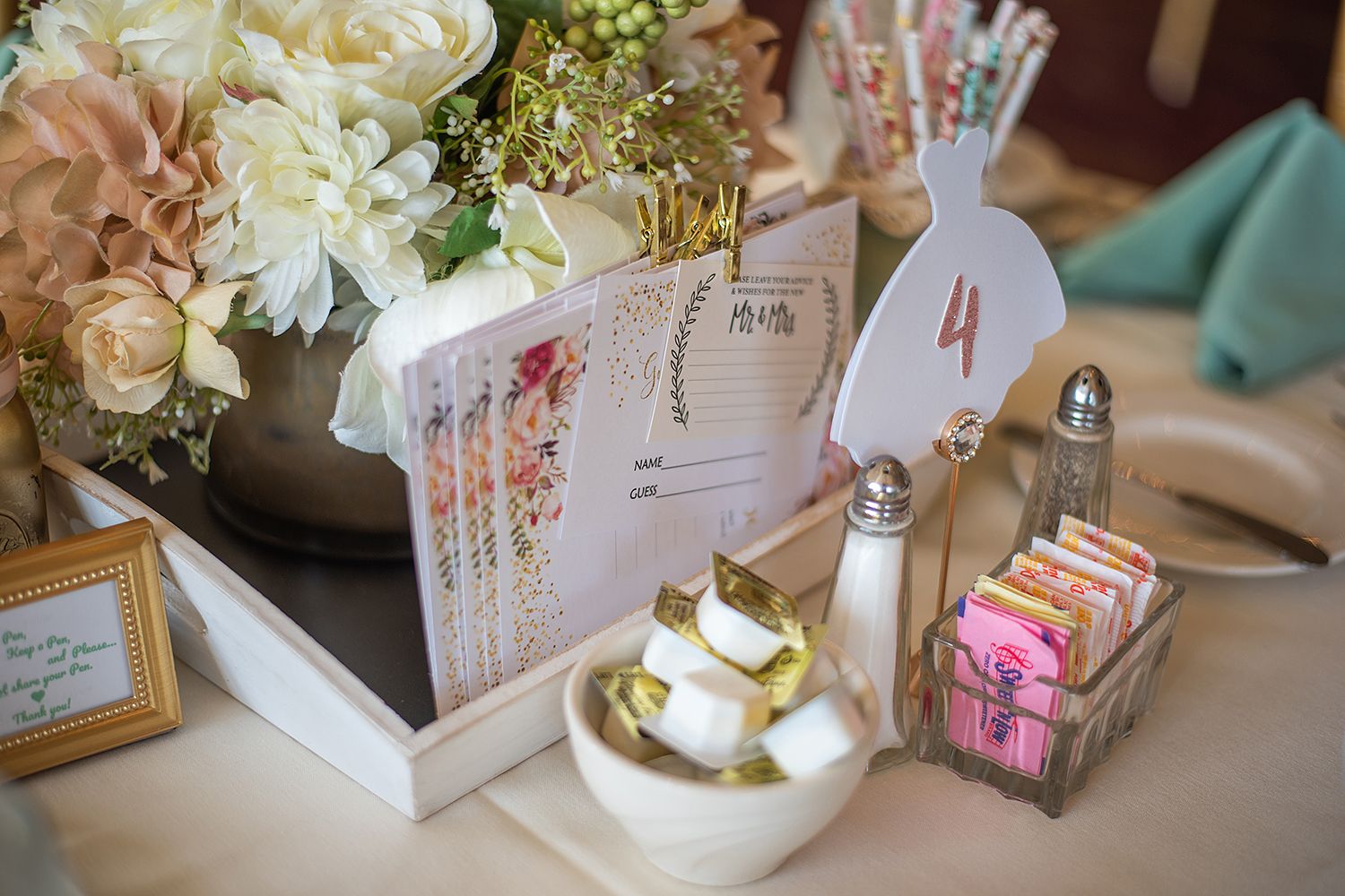Elegant wedding reception table display with gold accents, white flowers, and table numbers in ornate frames.