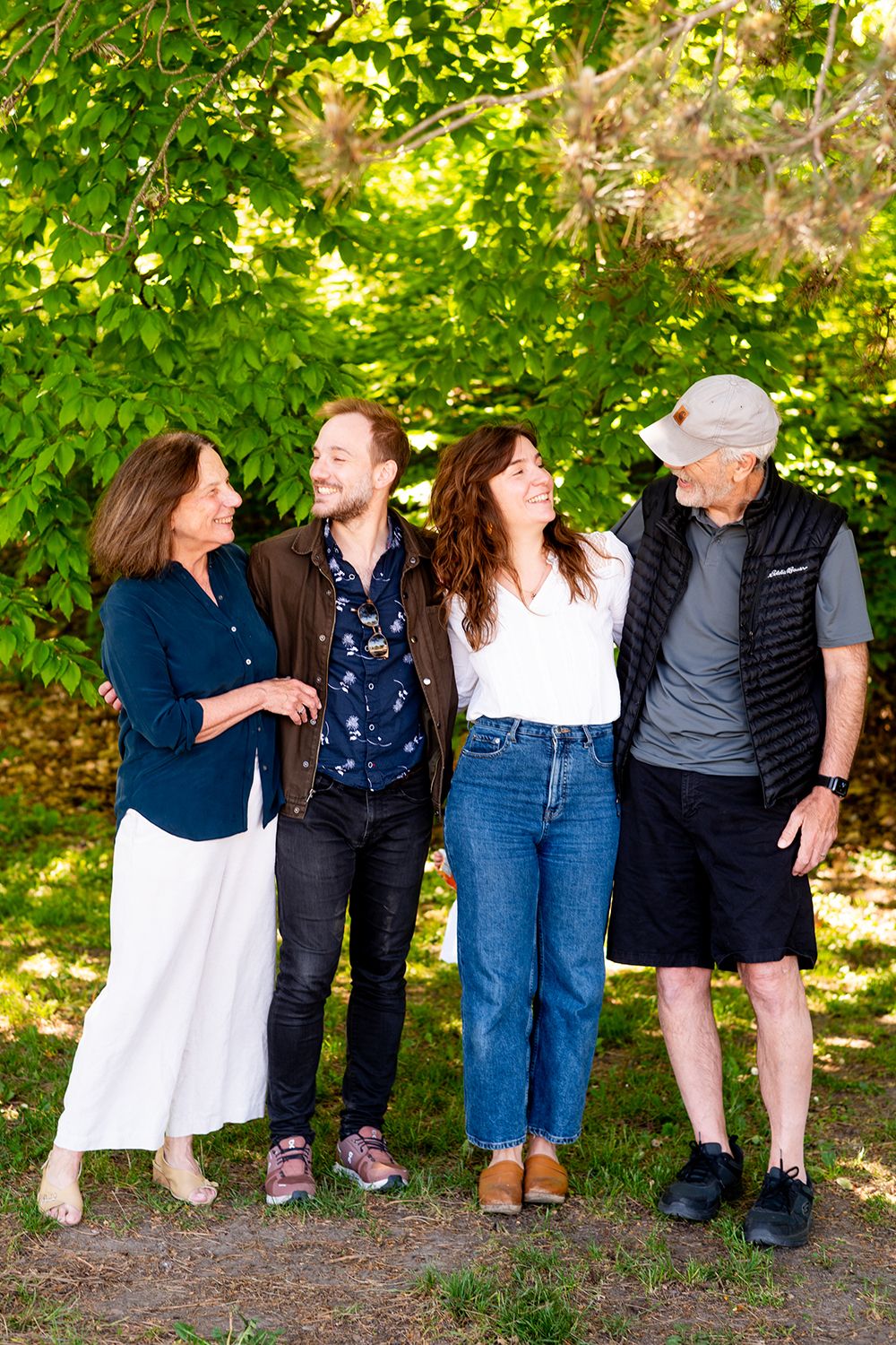 Family group laughing together while standing on a forest path under dappled sunlight.