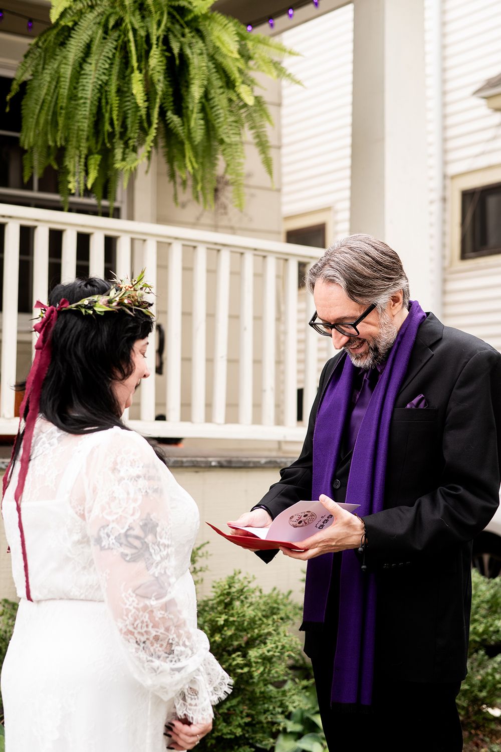An intimate outdoor wedding ceremony with lace dress details and purple clergy stole under a hanging fern.
