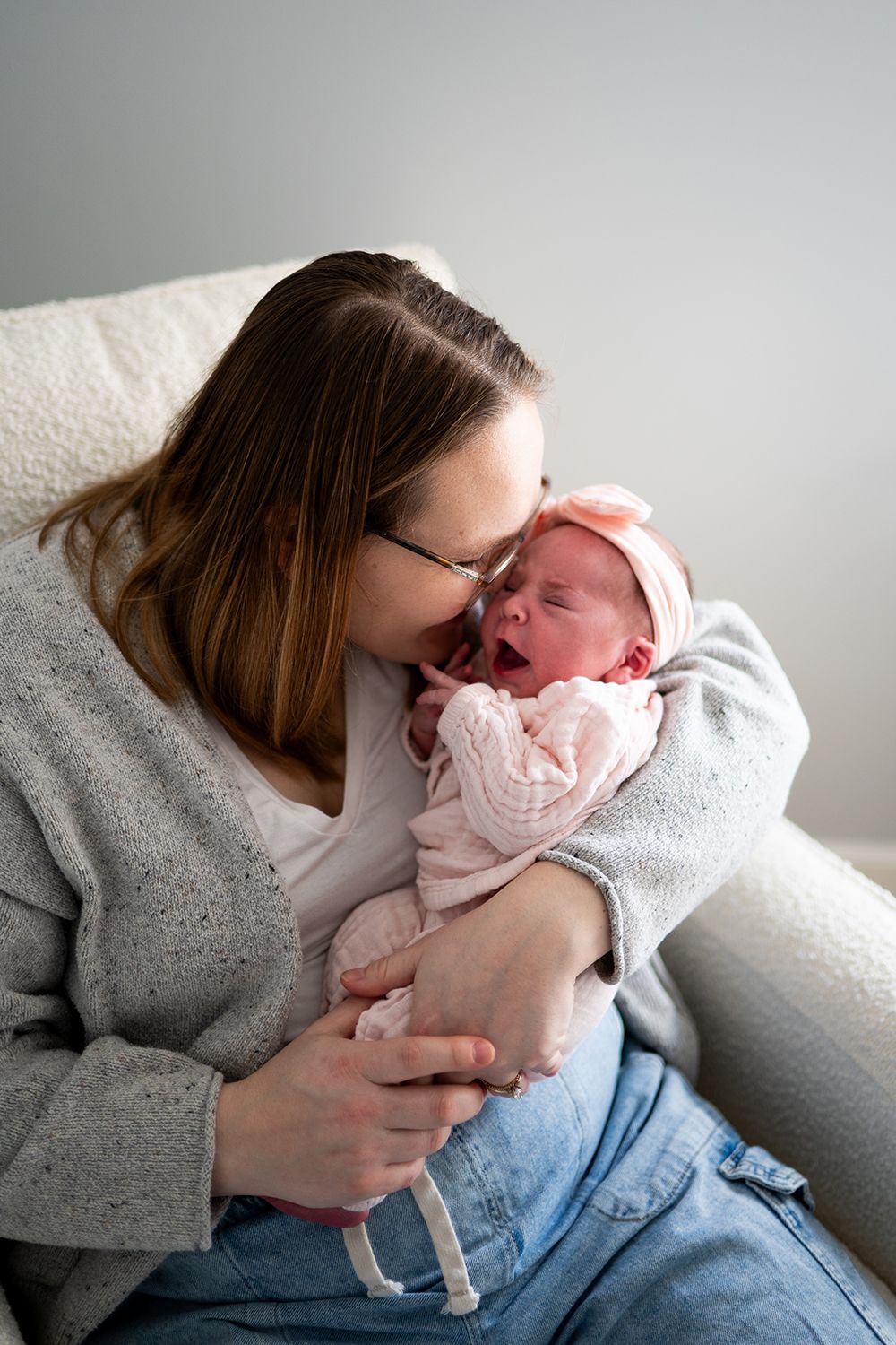 A tender moment captured as a parent in a gray sweater cuddles their newborn baby on a white couch.