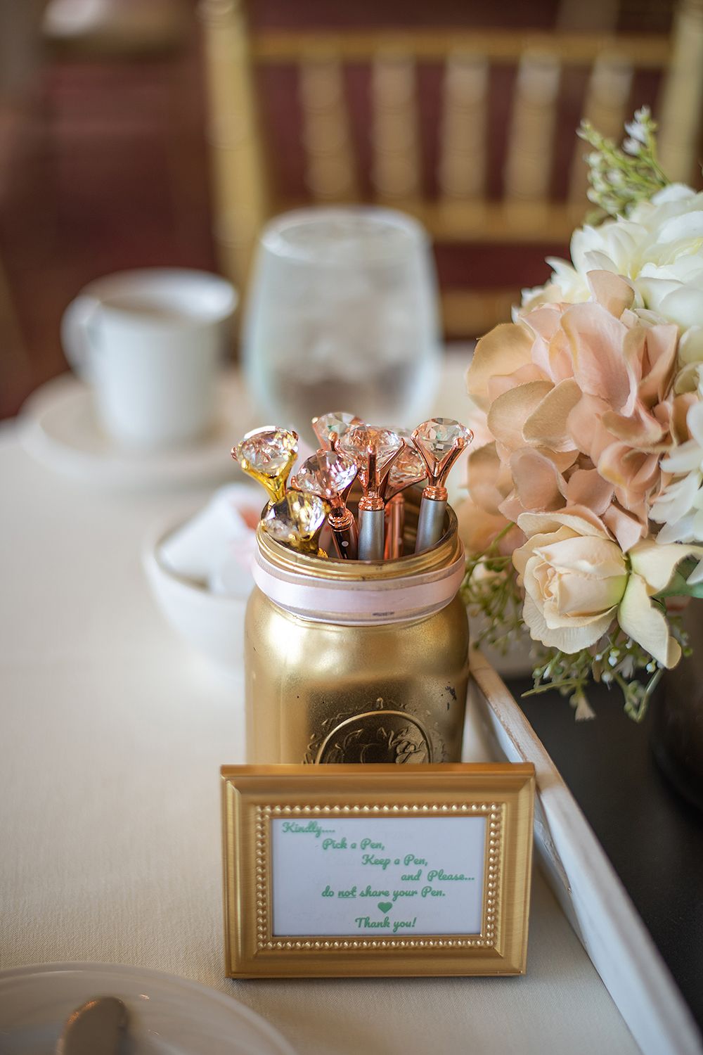 Close-up of gold framed table cards and decorative jars with pink floral accents at a wedding reception.