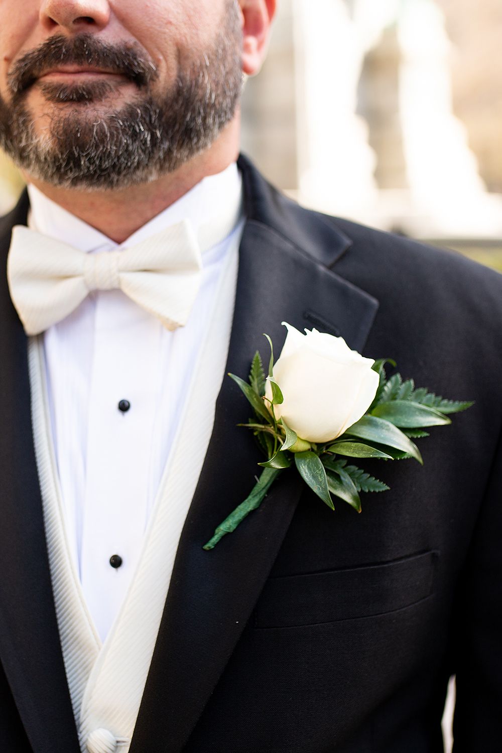 Close up view of groomsmen wearing classic black tuxedos with white bowties and white rose boutonnieres.