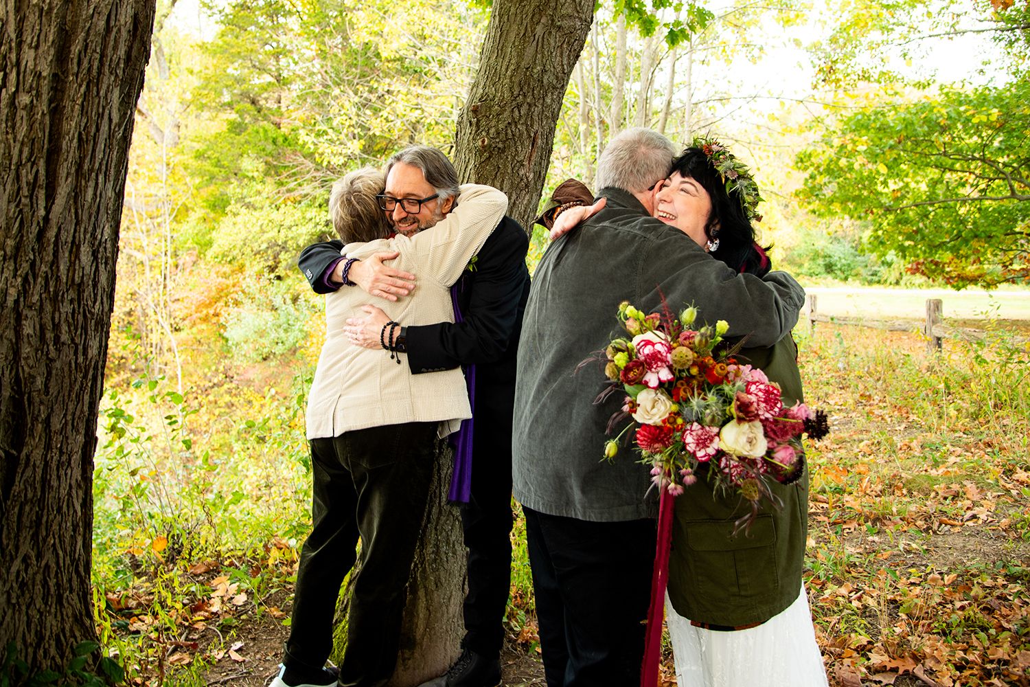Wedding party members share emotional embraces during an outdoor fall ceremony.