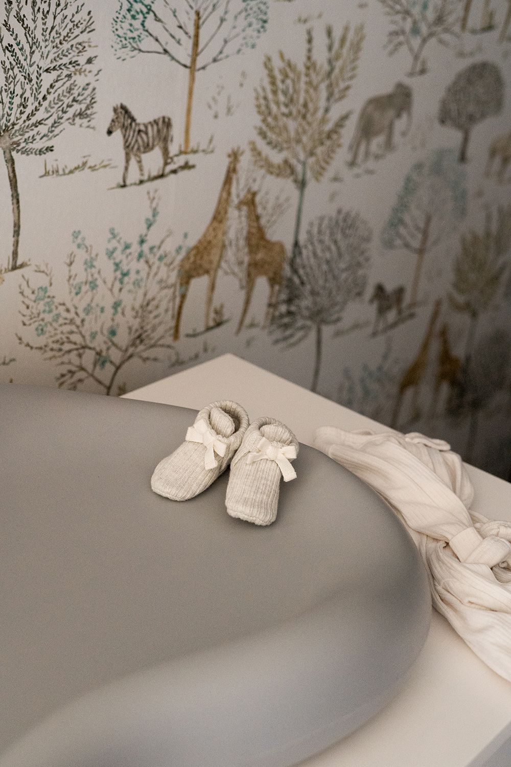 Small white baby booties displayed against gray surface with safari animal wallpaper pattern in the background.