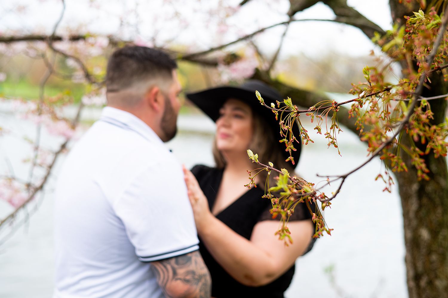 Couple embraces beneath flowering tree branches in a romantic outdoor engagement photo session.