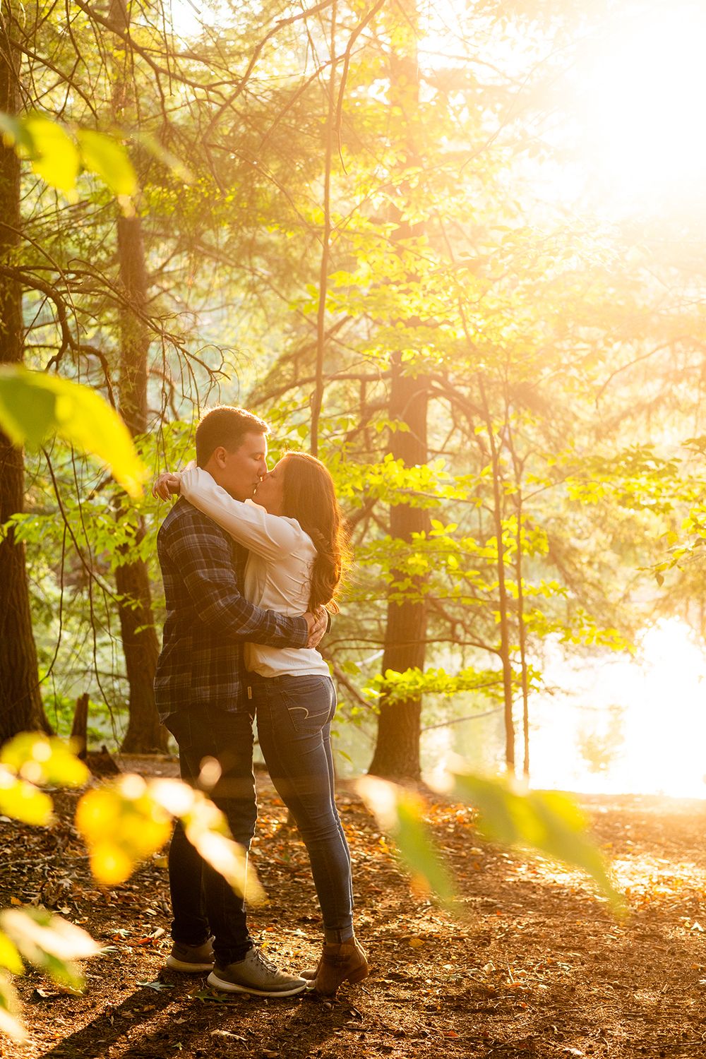 A couple embrace in a romantic autumn forest setting with golden sunlight streaming through the trees making a dreamy scene.