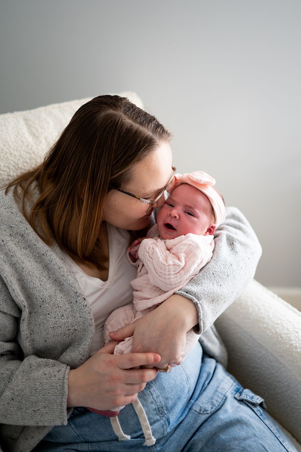 Parent lovingly embraces and kisses a swaddled newborn while sitting in a comfortable armchair.