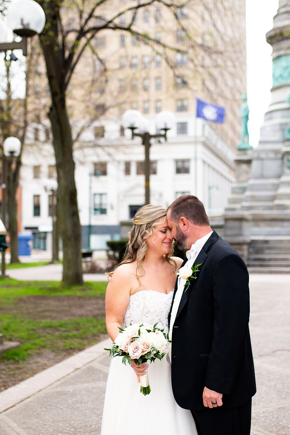 A romantic wedding moment captured in a city square with ornate architectural details and monuments.
