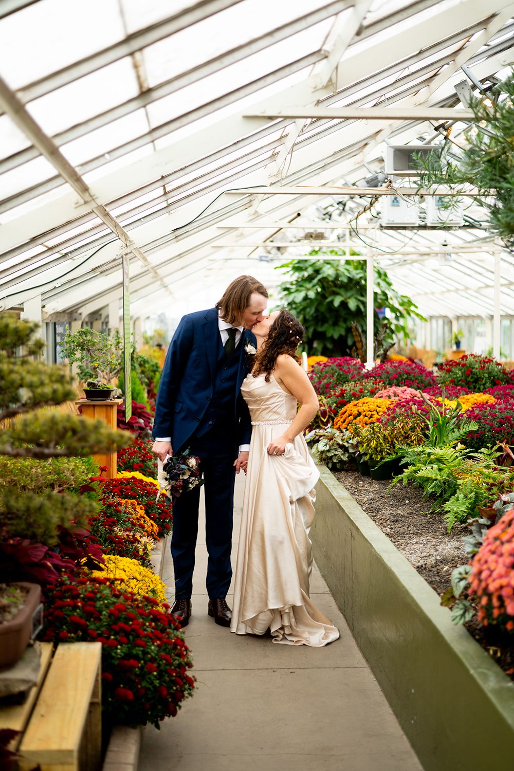 Newlyweds sharing intimate moments among vibrant flowers in a sunlit greenhouse.