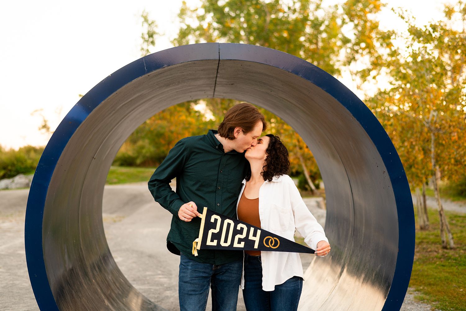 A couple poses together in a series of romantic engagement photos taken inside a large blue concrete tunnel at sunset.