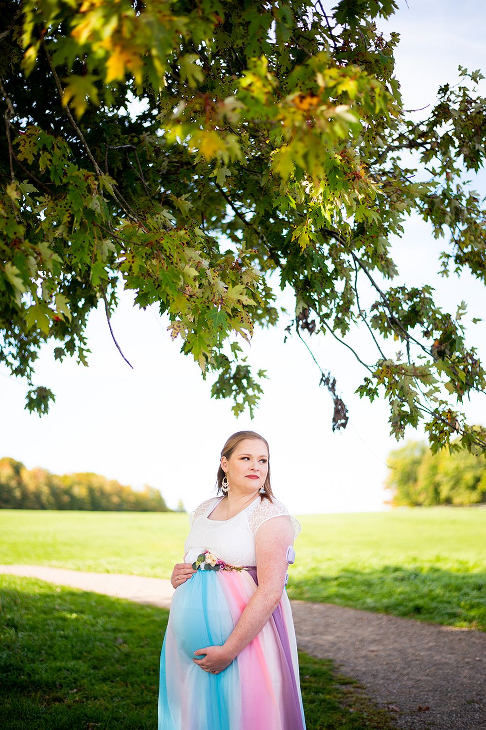 Woman in pastel dress runs joyfully through a park path under vibrant autumn maple leaves in golden sunlight.