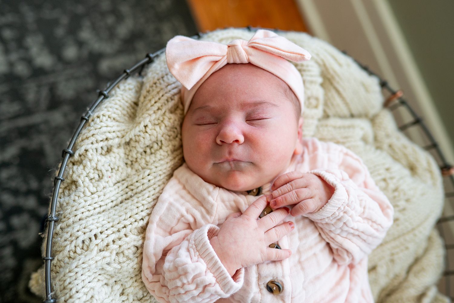 Peacefully sleeping newborn wearing soft pink knit outfit and matching headband rests on cream cable knit blanket.