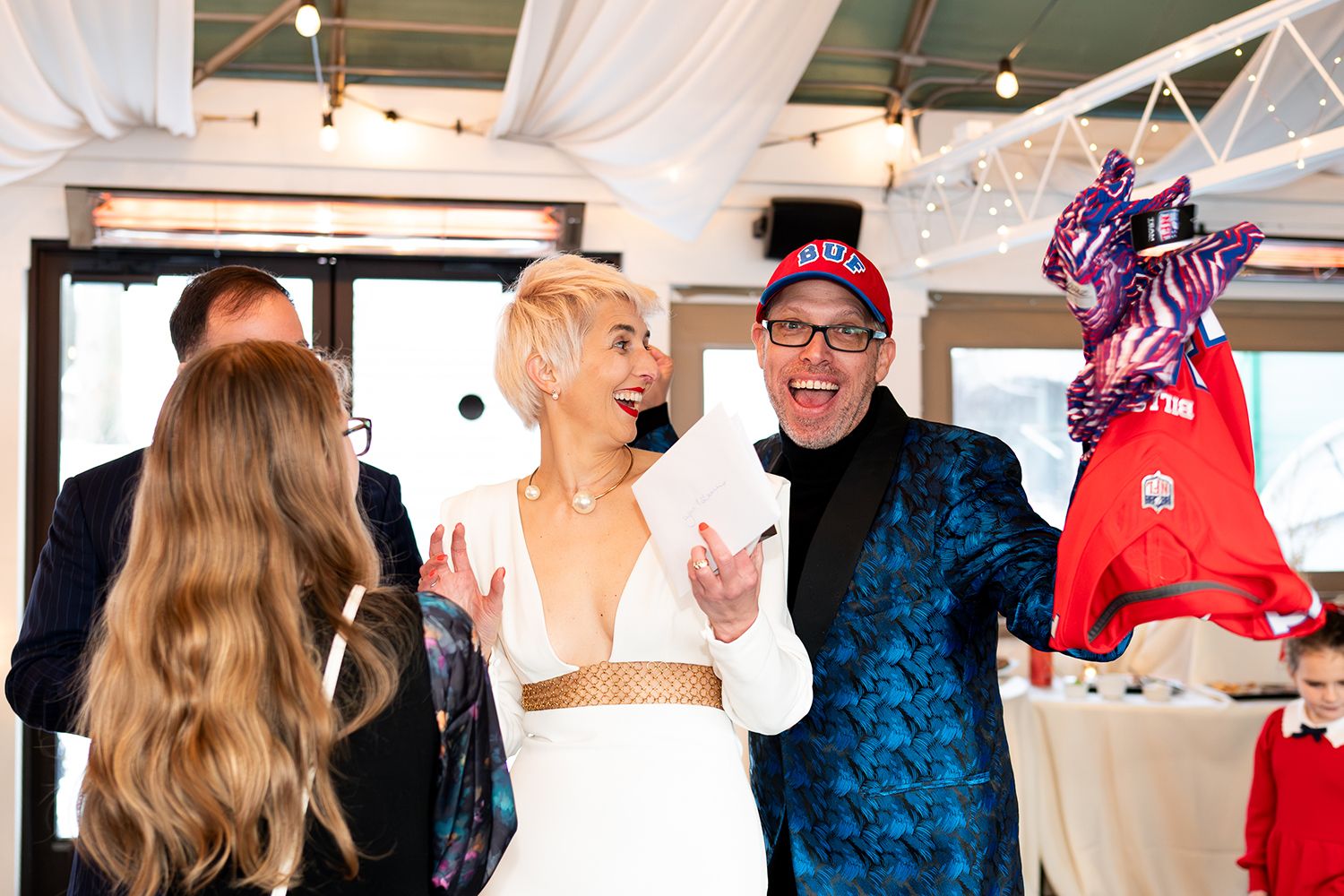 A joyful crowd celebrates with a couple during what appears to be a wedding reception indoors.