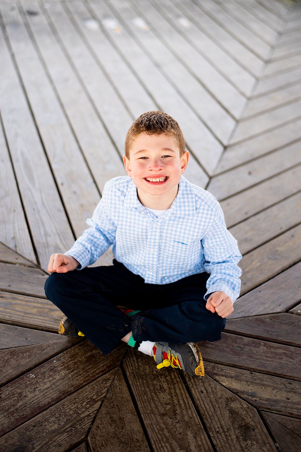 Cheerful pose sitting cross-legged on geometric wooden deck pattern.