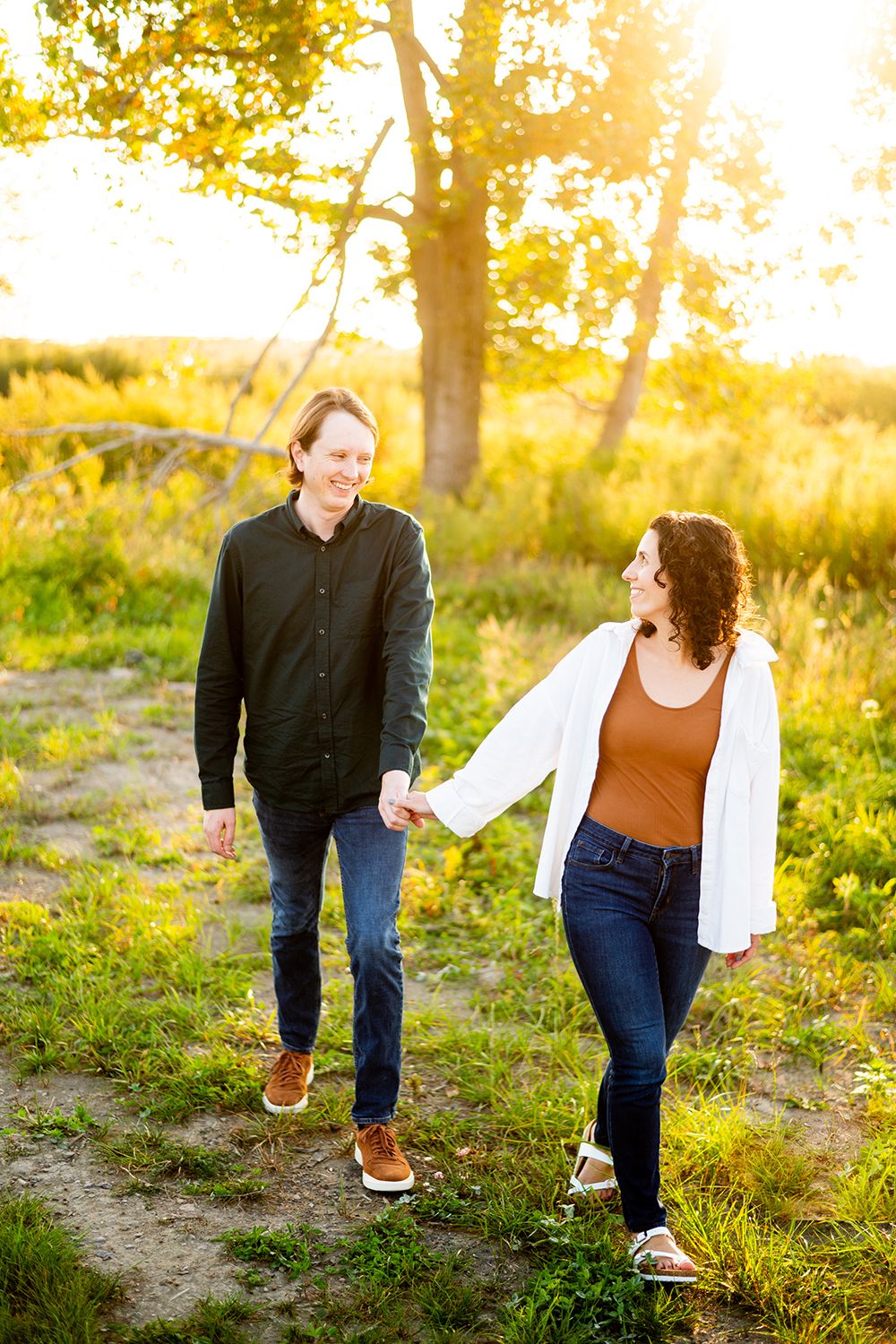 A couple walks hand in hand along a nature trail during golden hour sunset in autumn.