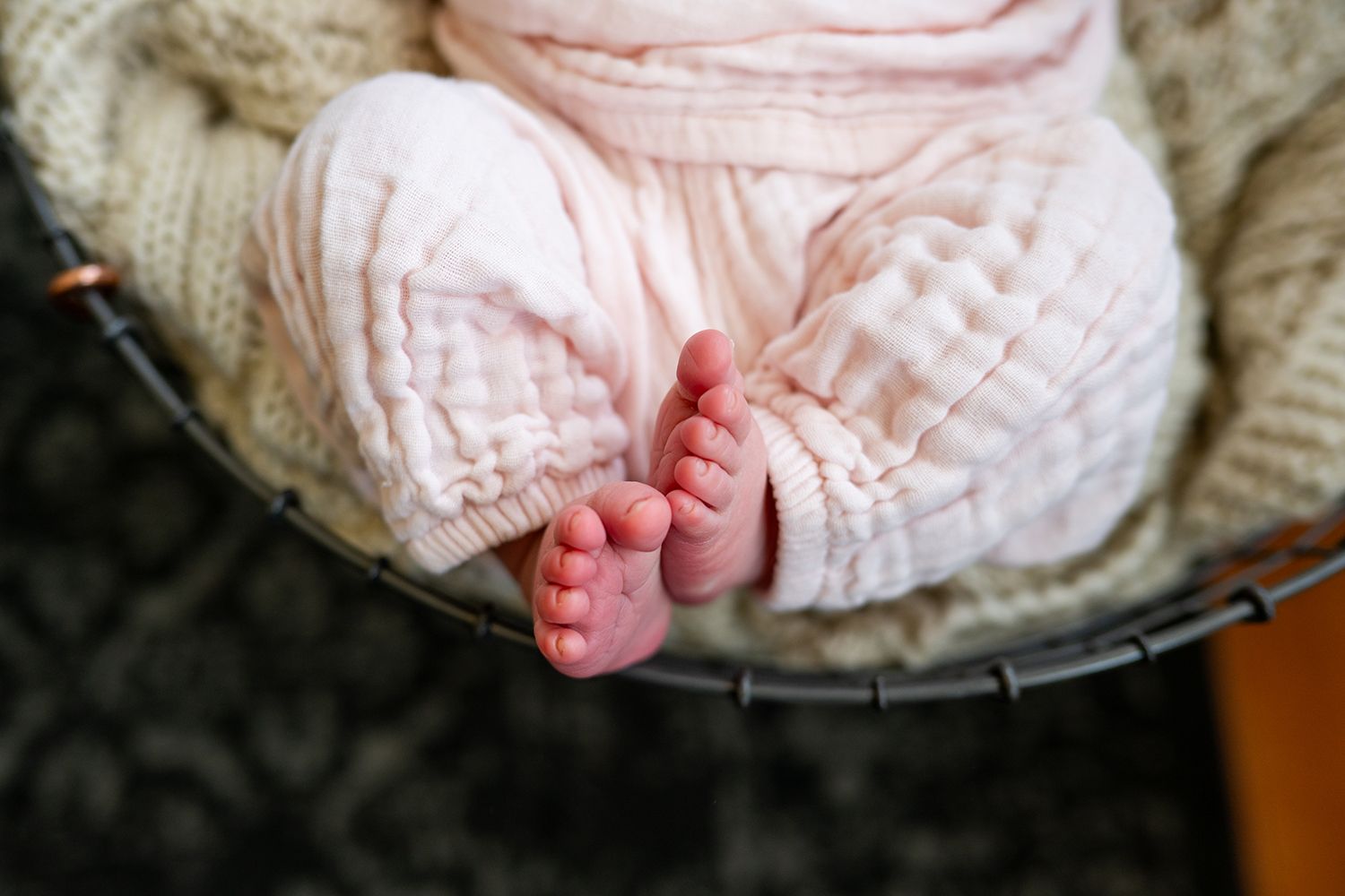 A tiny baby's foot wrapped in soft pink and white knit blanket resting on a neutral background.
