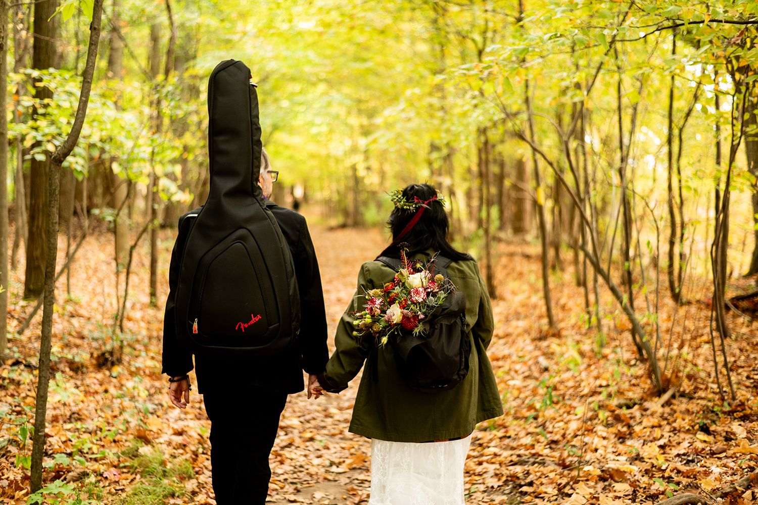 Two people holding hands while hiking through a colorful autumn forest with fallen leaves on the ground.