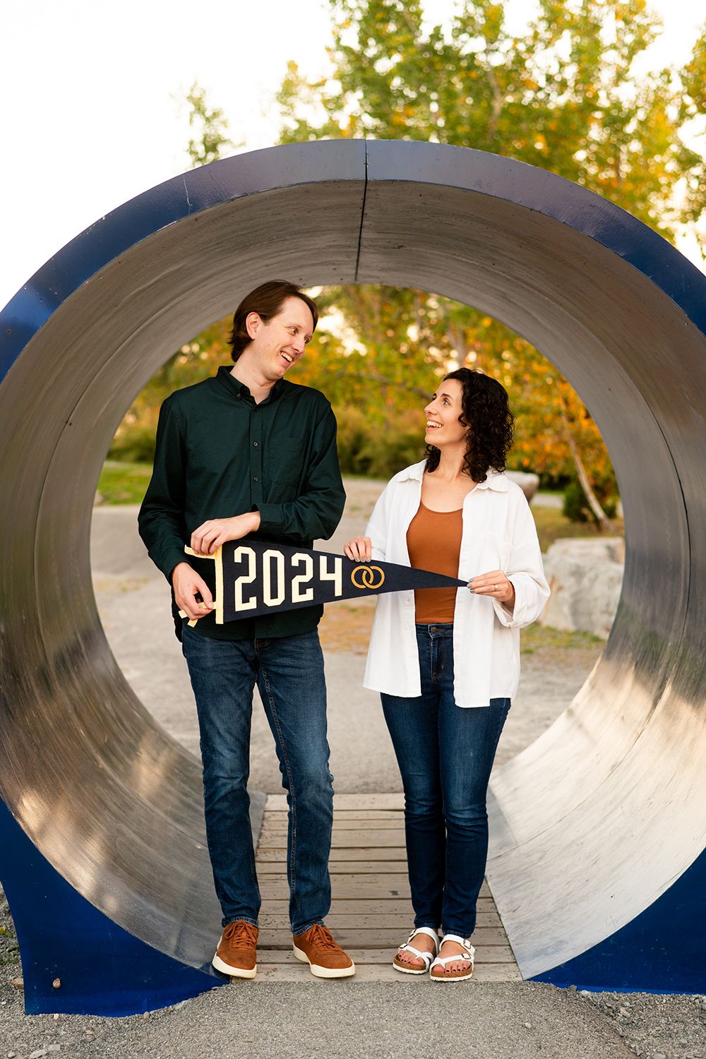 A couple poses with a 2024 sign inside a large blue tunnel structure during a sunset photo session.
