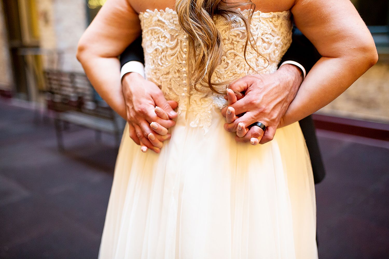 Close-up of hands adjusting back of ornate beige lace wedding dress with delicate embroidered details.
