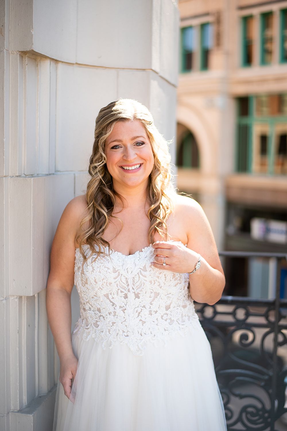 A person in a white lace wedding dress poses against a column at an elegant outdoor venue.