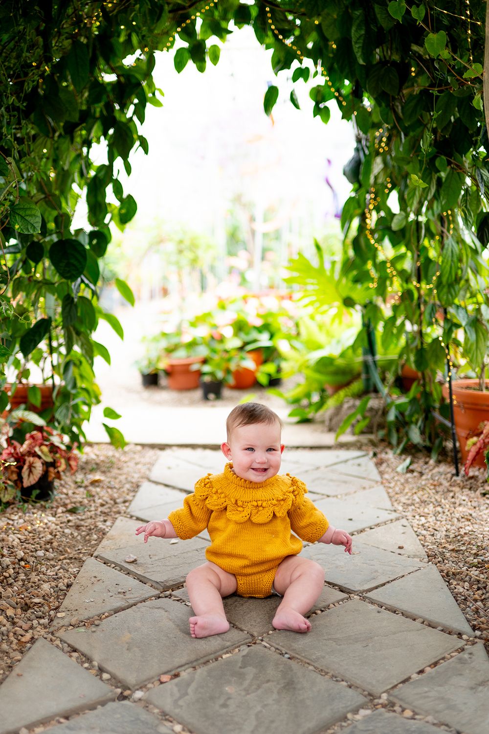 Four sequential photos of baby in yellow ruffled dress sitting on stone garden path surrounded by green plants.