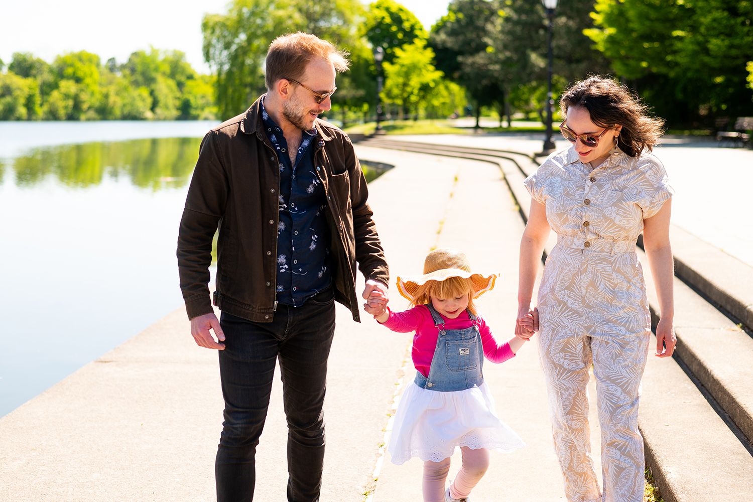 Couple walking with a young child along a waterfront path on a sunny day.