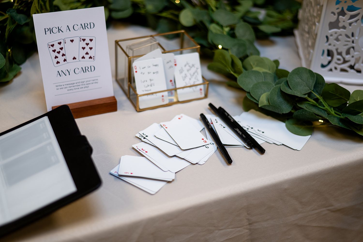 Place cards and table settings arranged on wooden surface with green foliage in background.