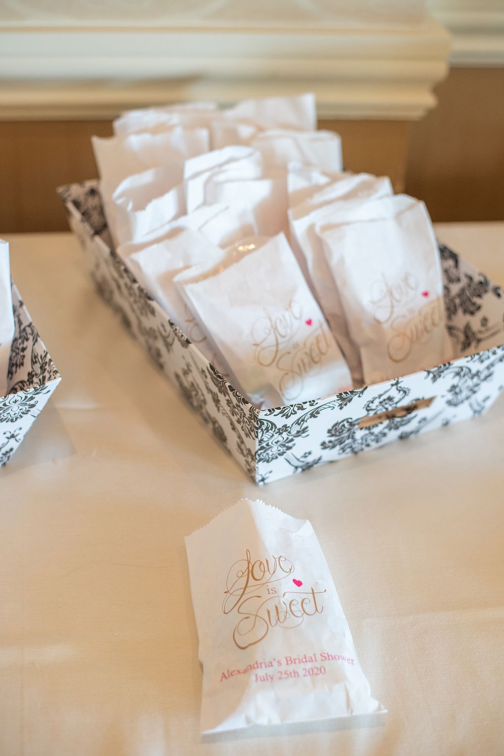 White favor bags with 'Love is Sweet' text arranged in a patterned box for a wedding celebration.