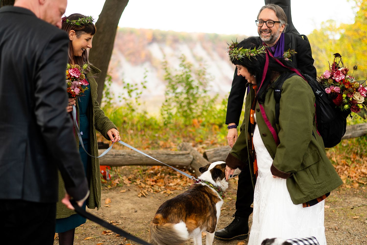 Pet dog walking with couple on woodland trail during autumn engagement photography session.