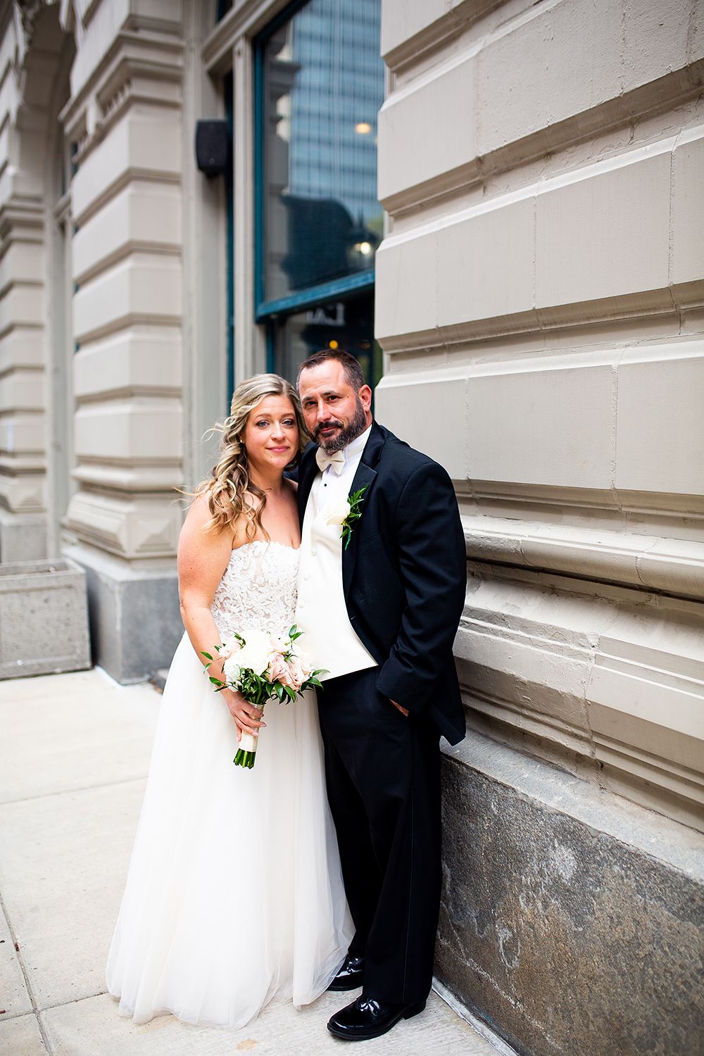 A bride and groom share intimate moments against a classical stone building facade in a wedding photo series.