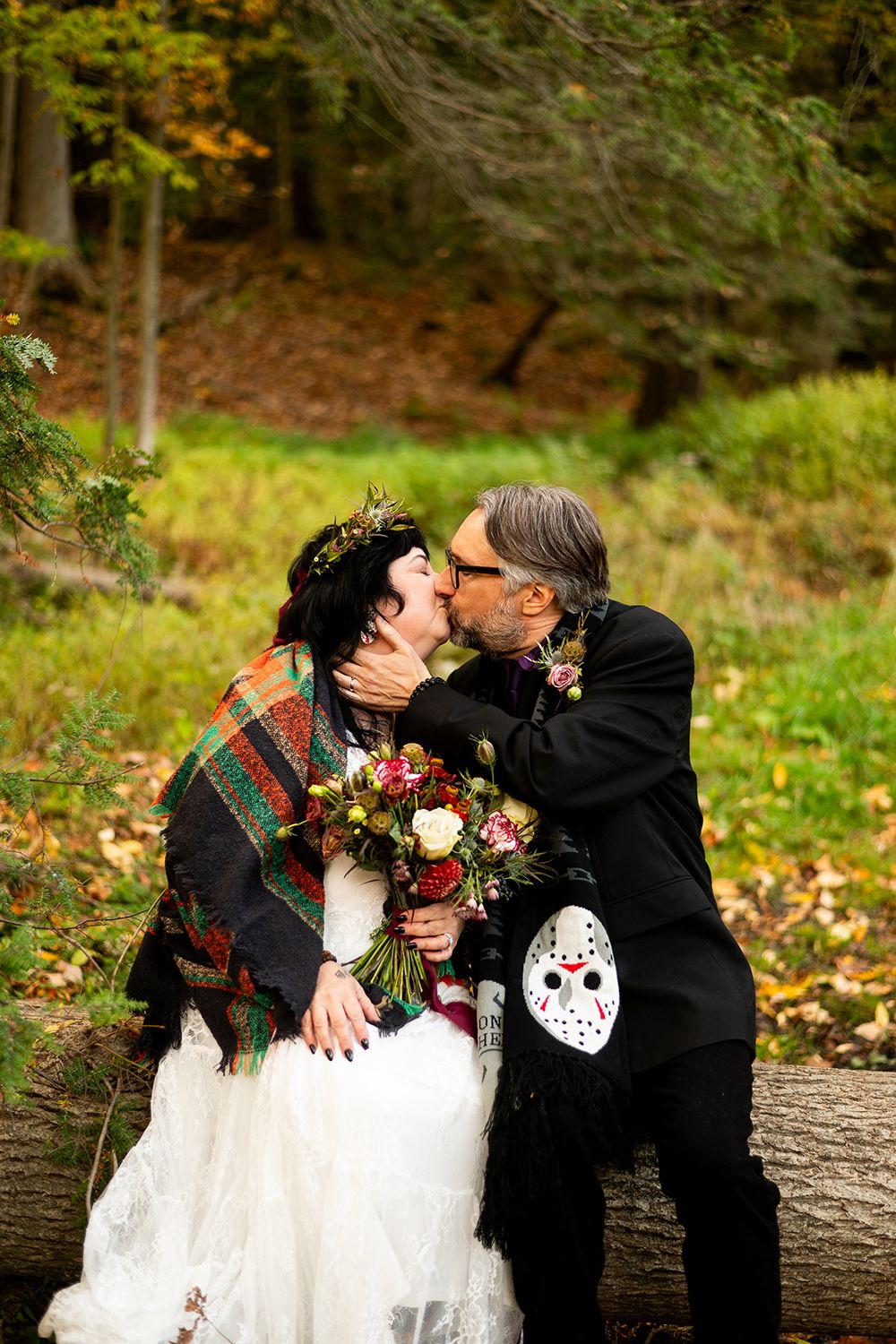 A romantic Halloween-themed wedding photoshoot in a forest with fallen autumn leaves and spooky decor.